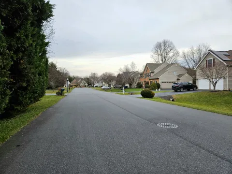 A quiet residential street with homes and lawns on an overcast evening